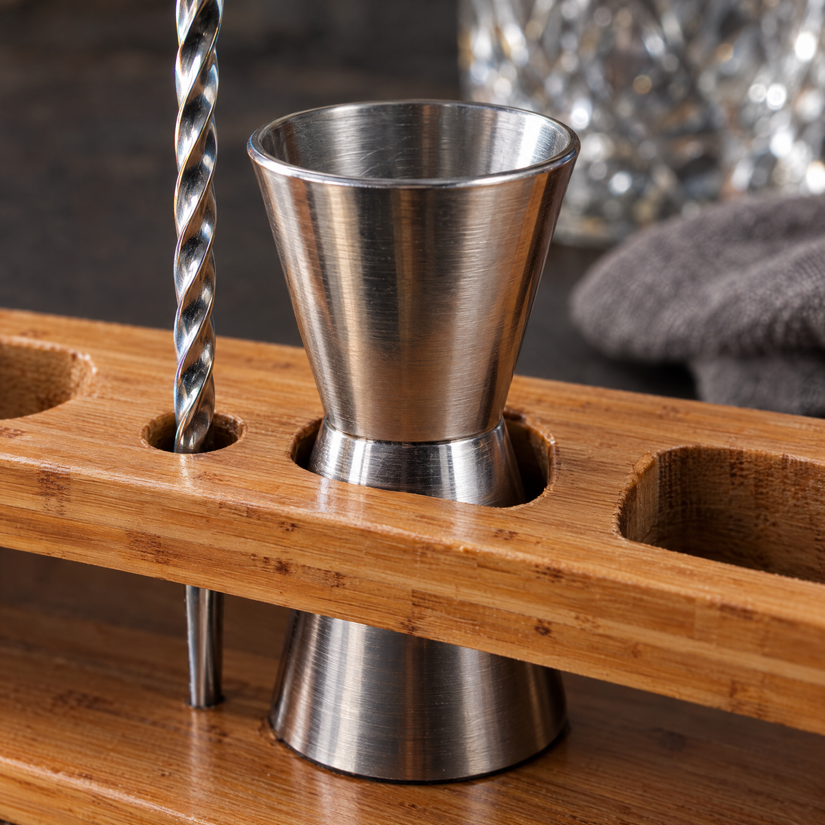 Close-up of the bamboo stand's cut slots with the jigger and bar spoon seated in them