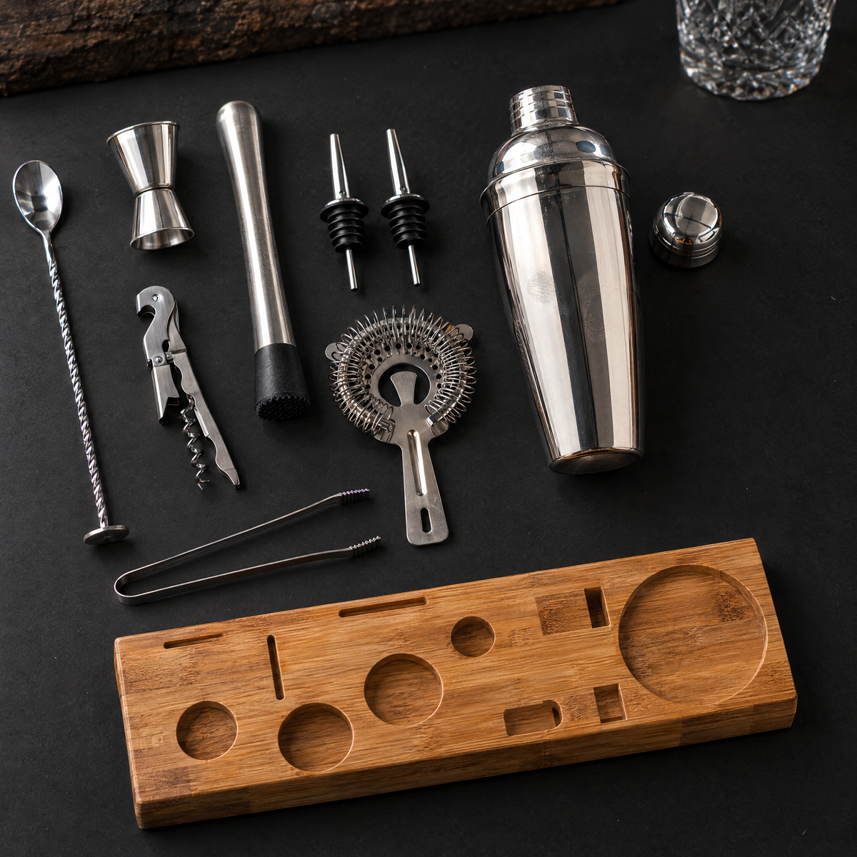 All ten pieces laid out flat: shaker, strainer, jigger, bar spoon, muddler, corkscrew, tongs, two pourers and the bamboo stand