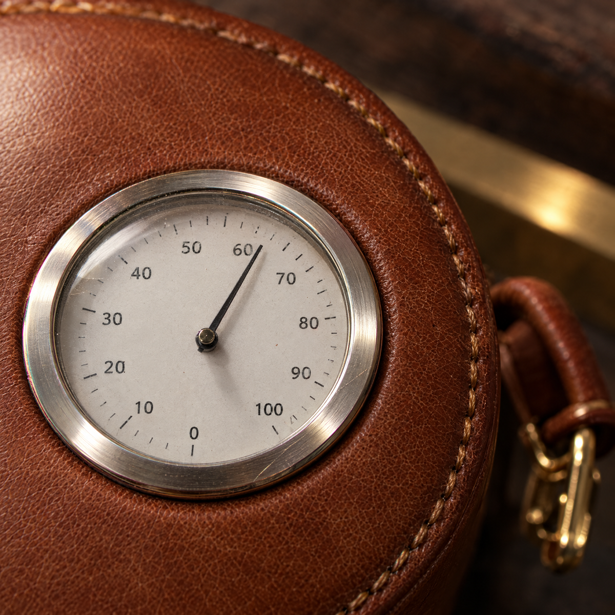 Close-up of the analogue hygrometer dial set into the leather lid behind a chrome bezel