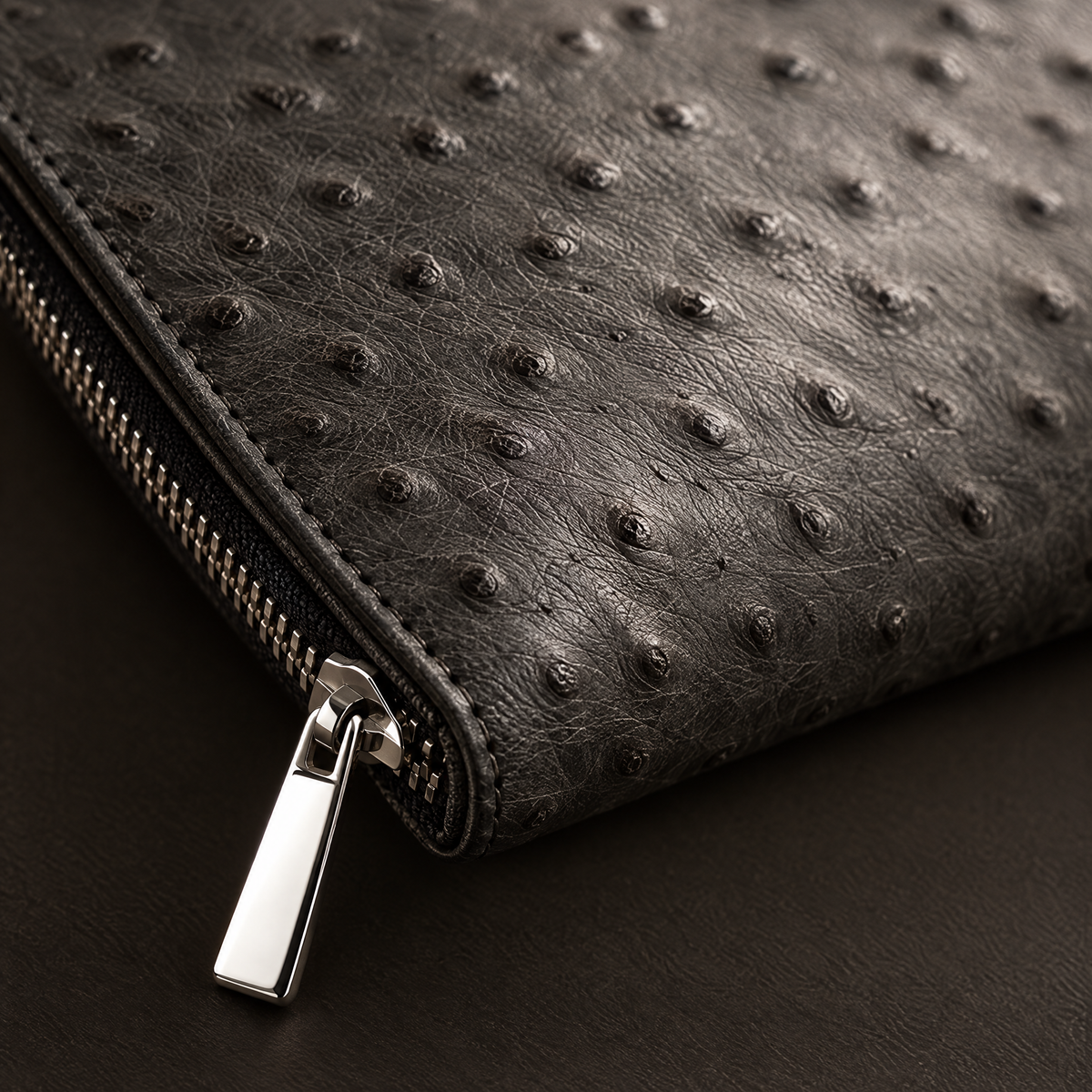 Macro detail of the ostrich-grain leather and polished zip pull of the Consul Reserve case